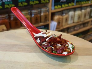 Condimento Arrabbiata: Cayenas secas en rodajas con hierbas aromáticas en una cuchara encima de una tabla de madera