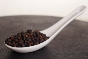 Granos de pimienta negra en una cuchara de porcelana en la tienda de especias Sally Pepper en Madrid