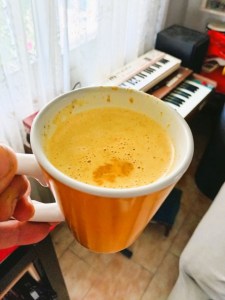 Taza de cristal de golden milk o también llamado Leche Dorada, sujetada por una mano y fondo un teclado musical