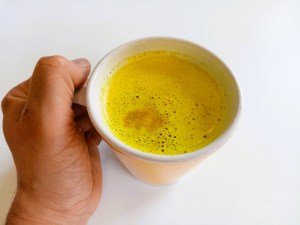 Taza de leche dorada sujetada por una mano